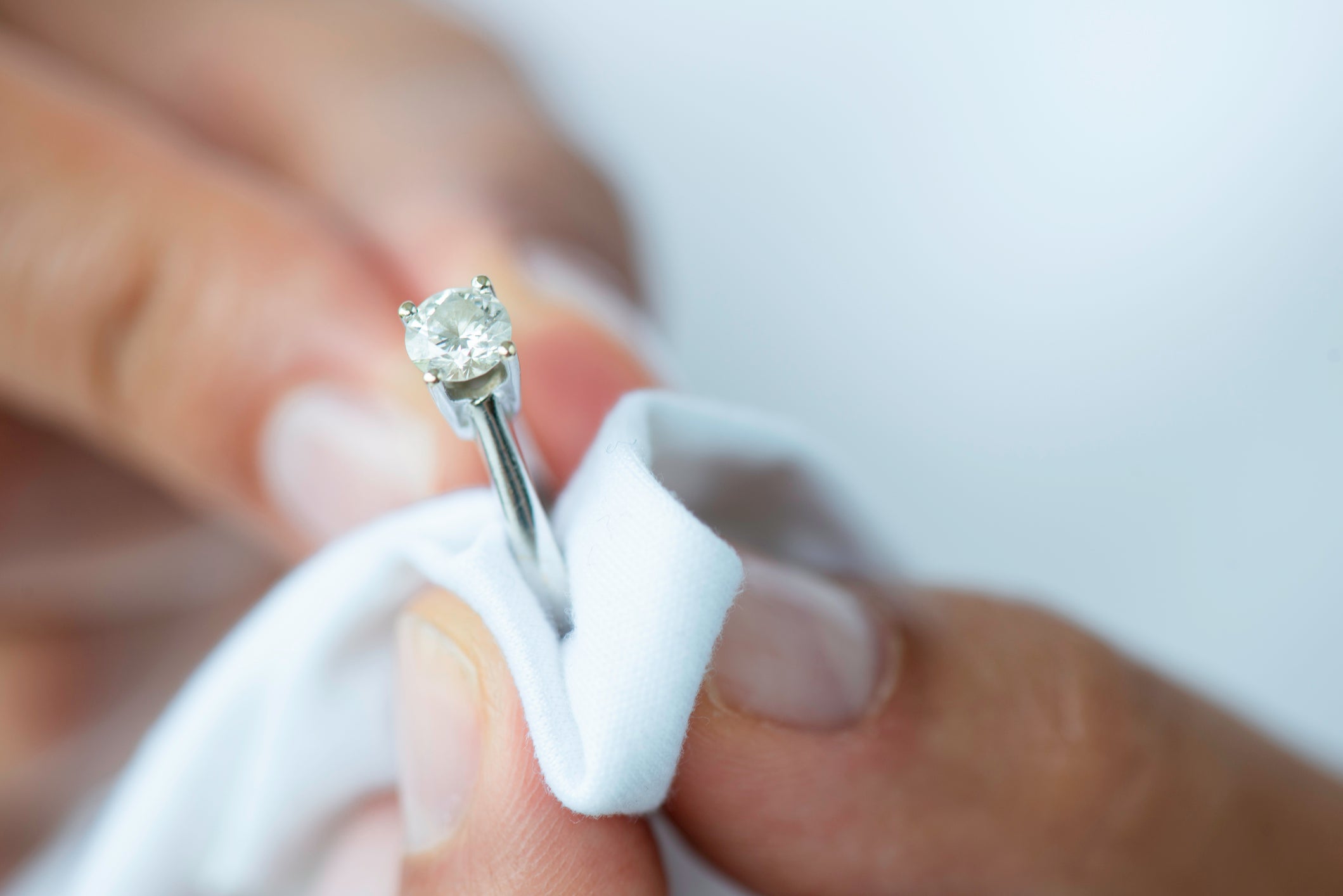 A close-up of a person cleaning a diamond ring with a soft white cloth