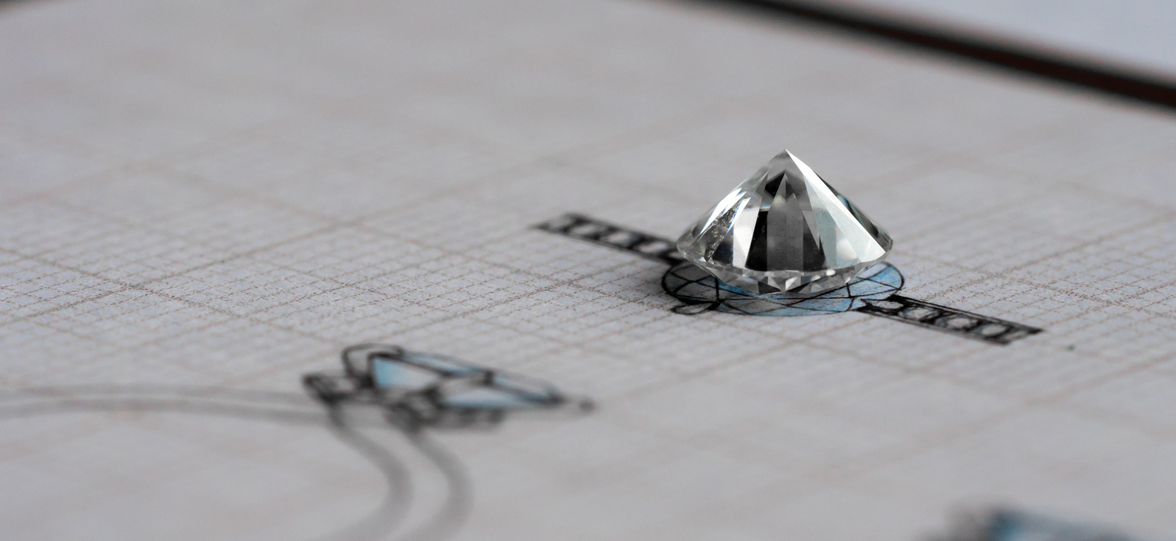 A loose diamond placed on a jewelry design sketch, showcasing detailed blueprints of a ring setting on graph paper.