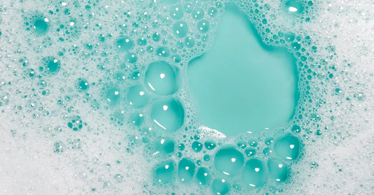A close-up of turquoise soapy water with bubbles forming a foamy texture