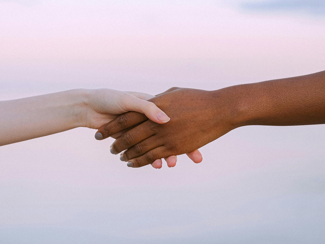 Two hands with different skin tones holding each other firmly at sunset, symbolizing unity, solidarity, and trust across differences.