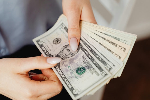 Close-up of a person’s hands fanning out U.S. dollar bills, showing a stack of cash held between manicured fingers.